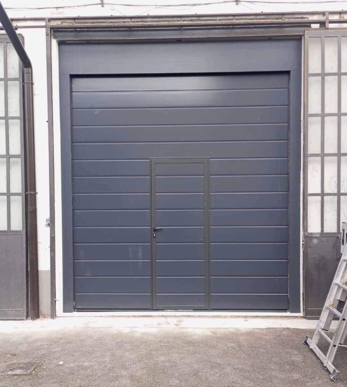 porta sezionale a <p>porta sezionale industriale in luce, con portina inserita e pannello con doga da 25cm. RAL 7016</p>
