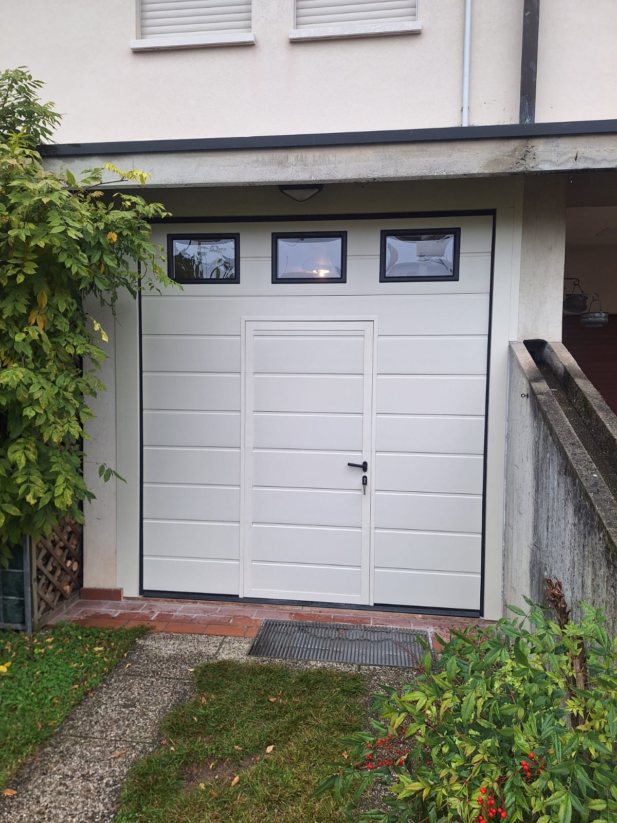 porta sezionale a <p>porta sezionale in luce, con coprifili, oblò, portina inserita e pannello con doga da 25cm. RAL 9020</p>