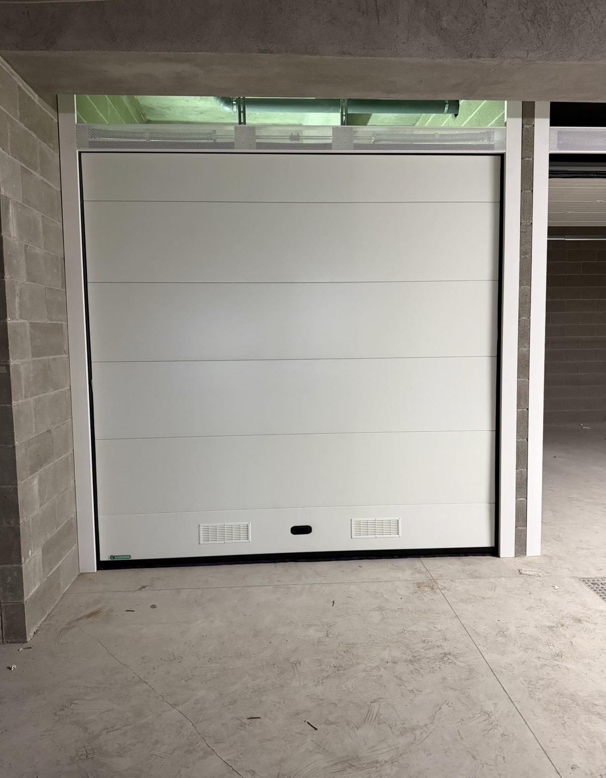 porta sezionale a <p>porta sezionale oltre luce, con veletta areata, maniglia di sollevamento, griglie di areazione e pannello intero. RAL 9010</p>