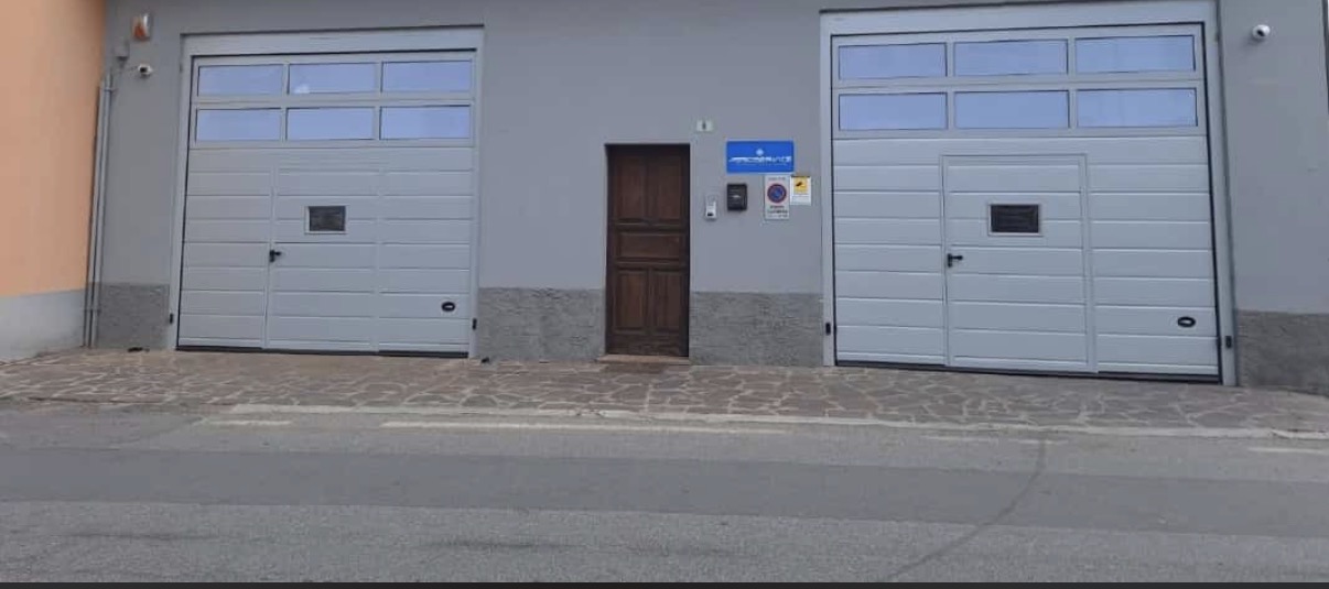 porta sezionale industriale a <p>porta sezionale industriale, con maniglia di sollevamento, portina inserita, fotocellule, lampeggiante e pannello con oblò. RAL 7035</p>