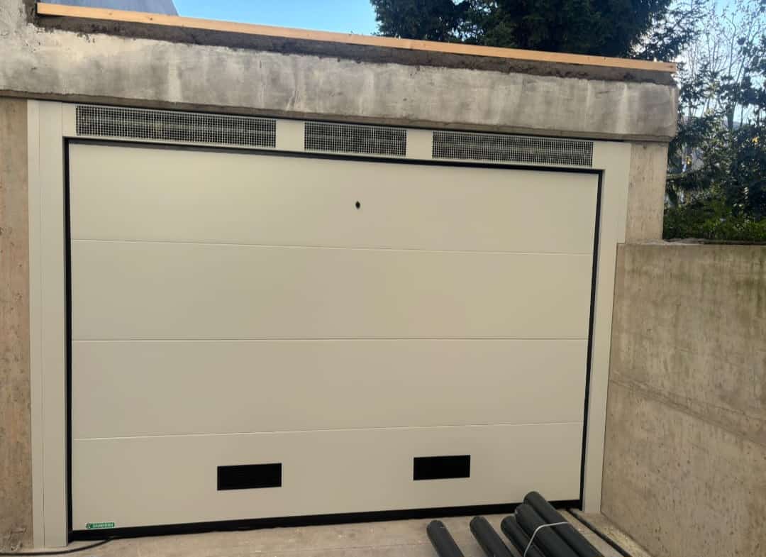 porta sezionale a <p>porta sezionale in luce, con veletta areata, griglie di areazione, sblocco esterno e pannello intero. RAL 9010</p>