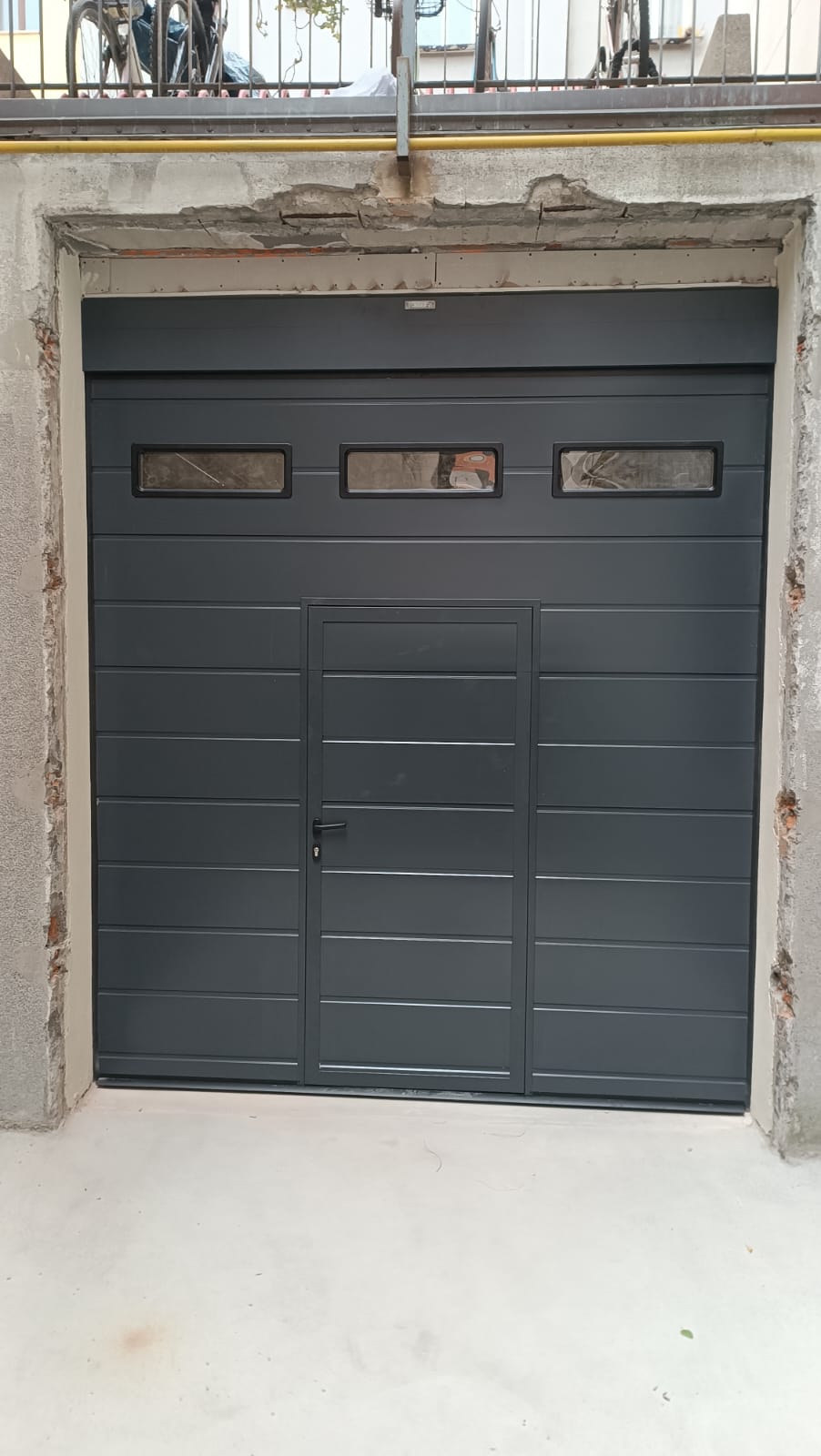 porta sezionale a <p>porta sezionale oltre luce, con tamponatura fissa, oblò, lampeggiante, portina inserita e pannello con doga da 25cm. RAL 7016</p>