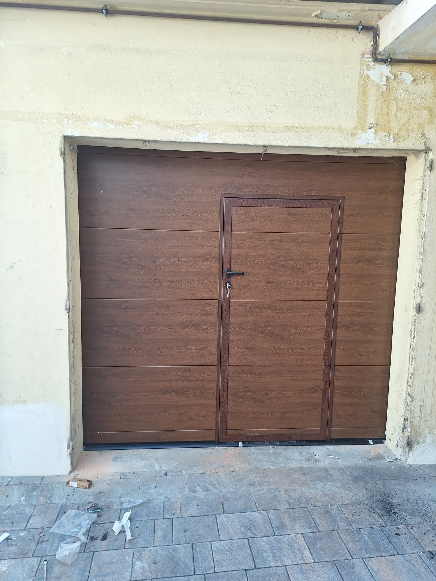 porta sezionale a <p>porta sezionale oltre luce, con portina inserita e pannello intero. Colore effetto legno scuro</p>