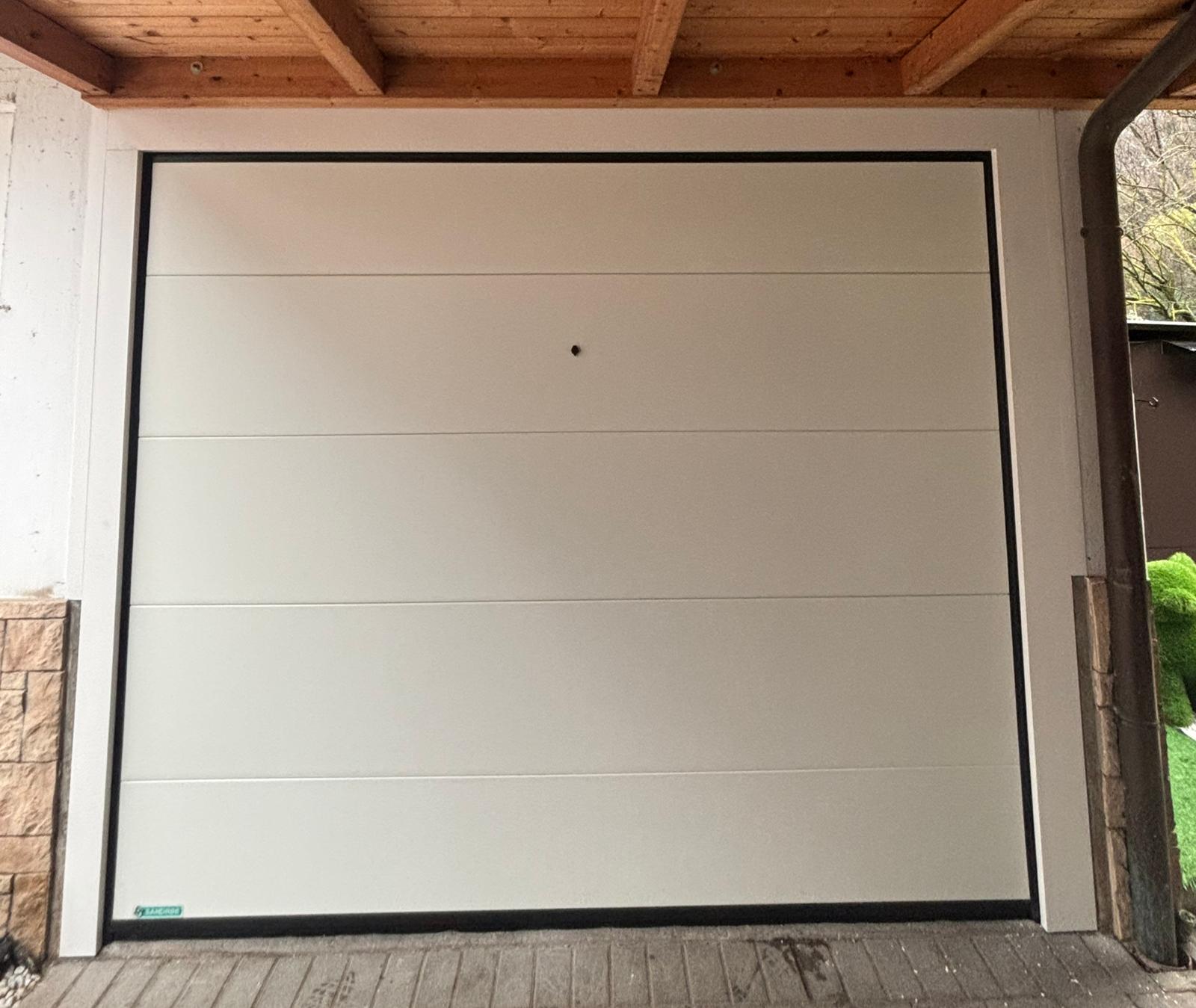 porta sezionale a <p>porta sezionale in luce, con coprifili, sblocco esterno e pannello intero. RAL 9010</p>