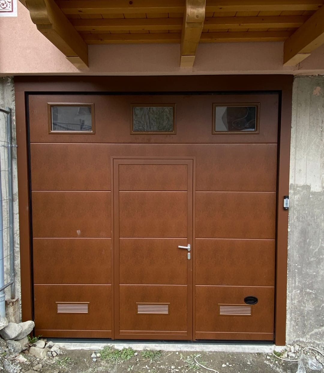 porta sezionale a <p>porta sezionale in luce, con griglie di areazione maniglia di sollevamento, portina inserita, oblò e telecodi. Colore effetto legno</p>