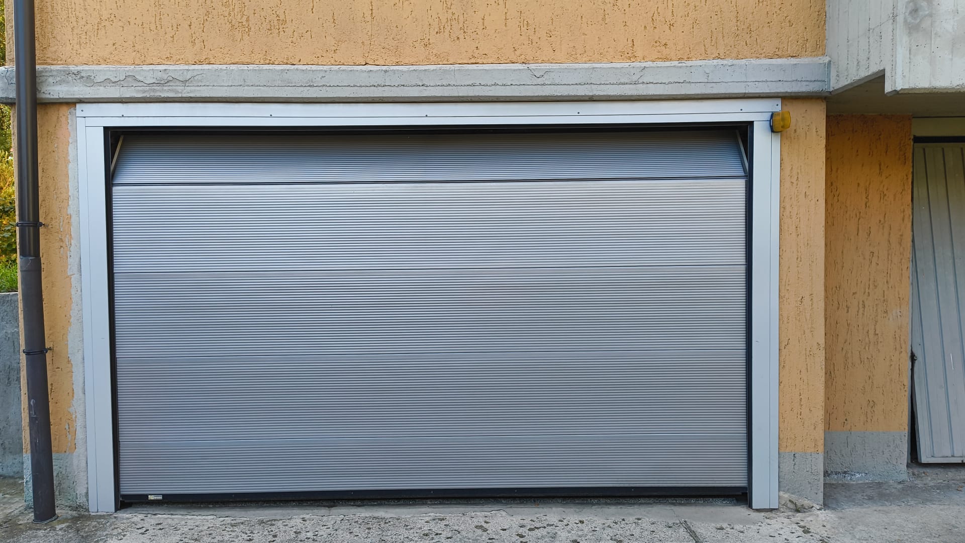 porta sezionale a <p>porta sezionale in luce, con coprifili, lampeggiante e pannello intero. RAL 9006</p>