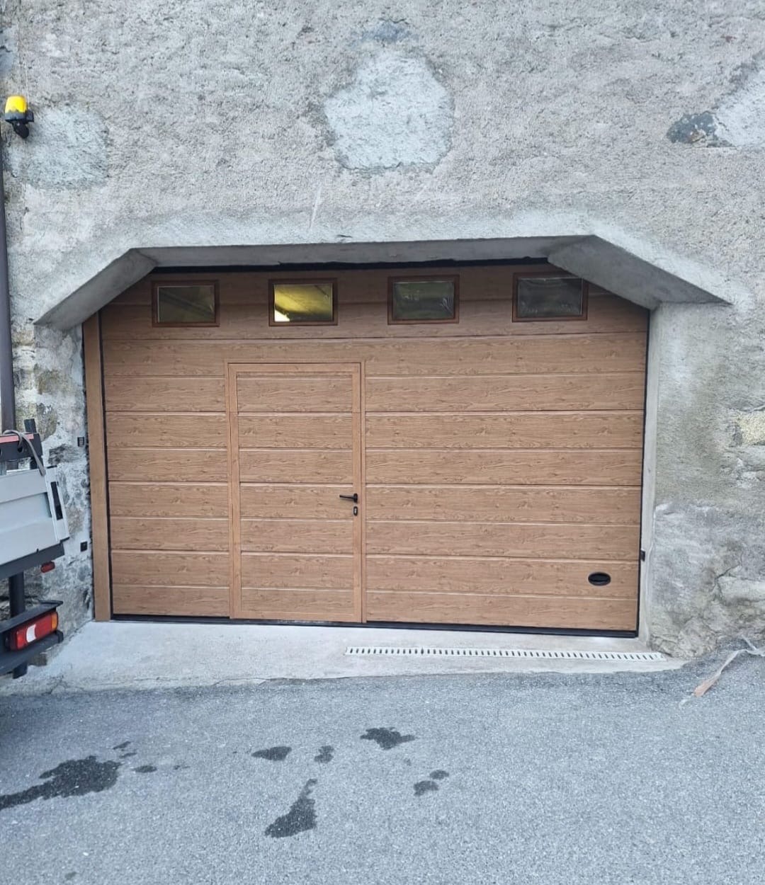 Porta sezionale a <p>Porta sezionale in luce, con oblò, maniglia di sollevamento, portina inserita e pannello con doga da 25cm. Colore effetto legno </p>