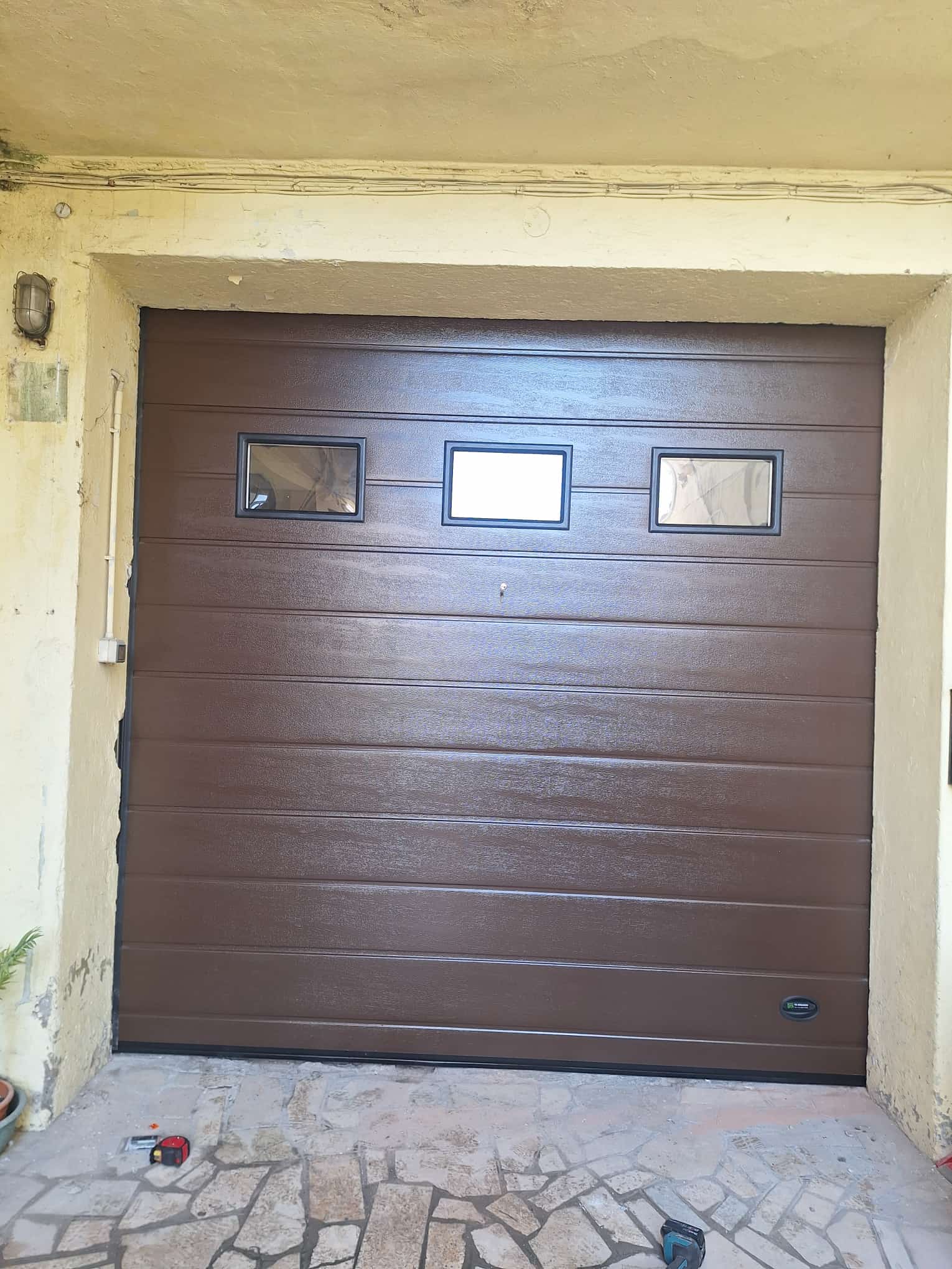 porta sezionale a <p>porta sezionale oltre luce, con sblocco esterno, maniglia di sollevamento, oblò e pannello con doga da 25cm. RAL 8014</p>