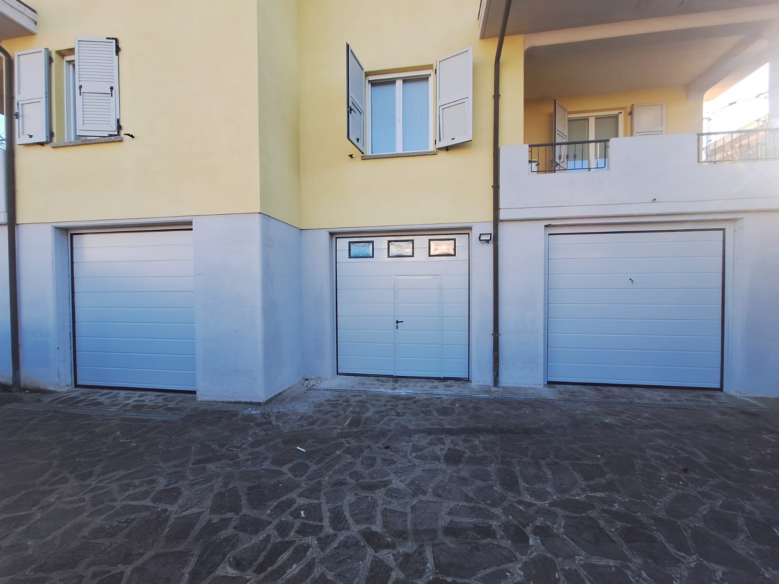 porta sezionale a <p>porta sezionale in luce, con oblò, portina inserita, sblocco esterno e pannello con doga da 25cm. RAL 7035</p>