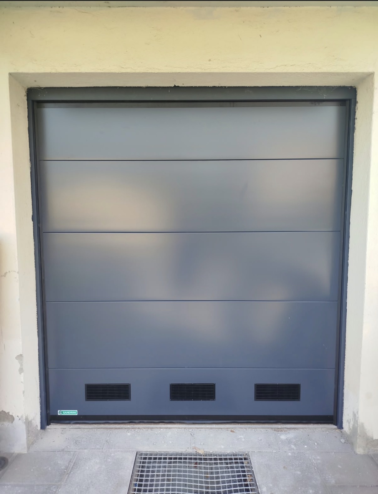 porta sezionale a <p>porta sezionale oltre luce, con griglie di areazione e pannello intero. RAL 7016</p>