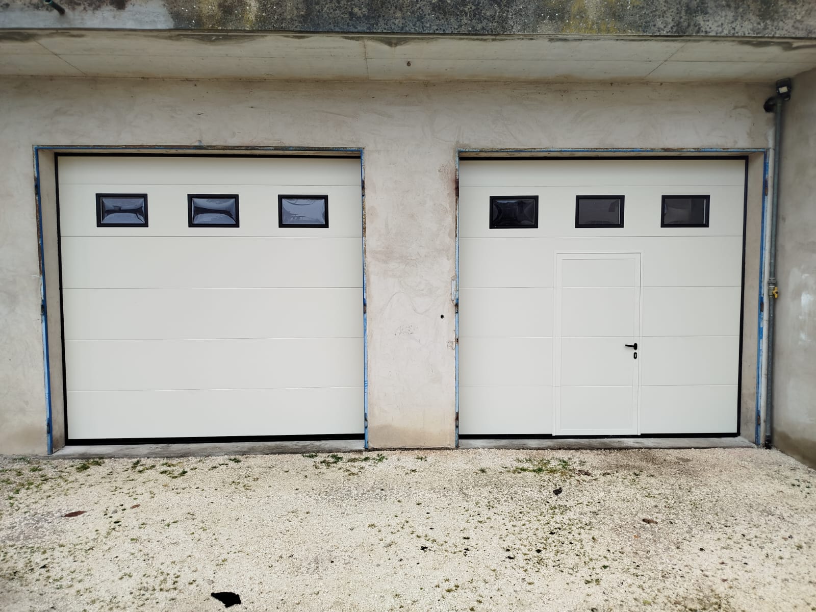 porta sezionale a <p>porta sezionale oltre luce, con oblò, portina inserita e pannello intero. RAL 9010</p>