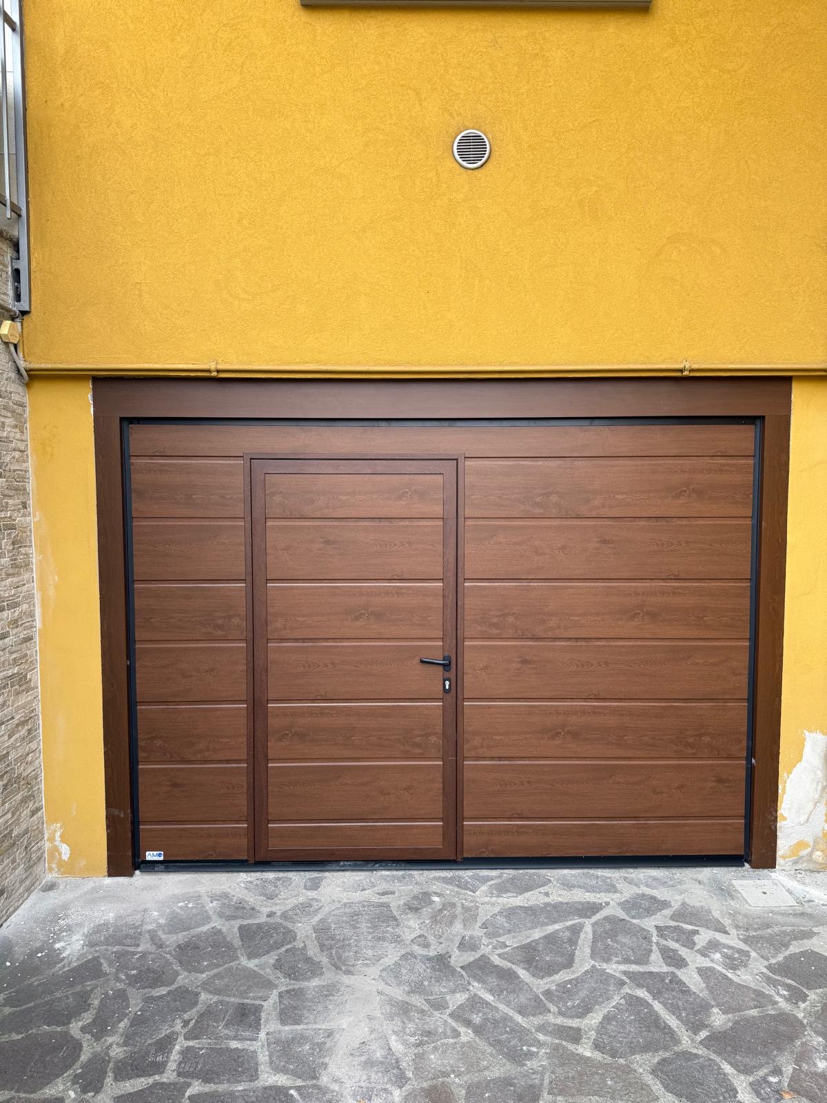 Porta sezionale a <p>Porta sezionale in luce, con portina inserita e pannello con doga da 25cm. Colore effetto legno scuro </p>