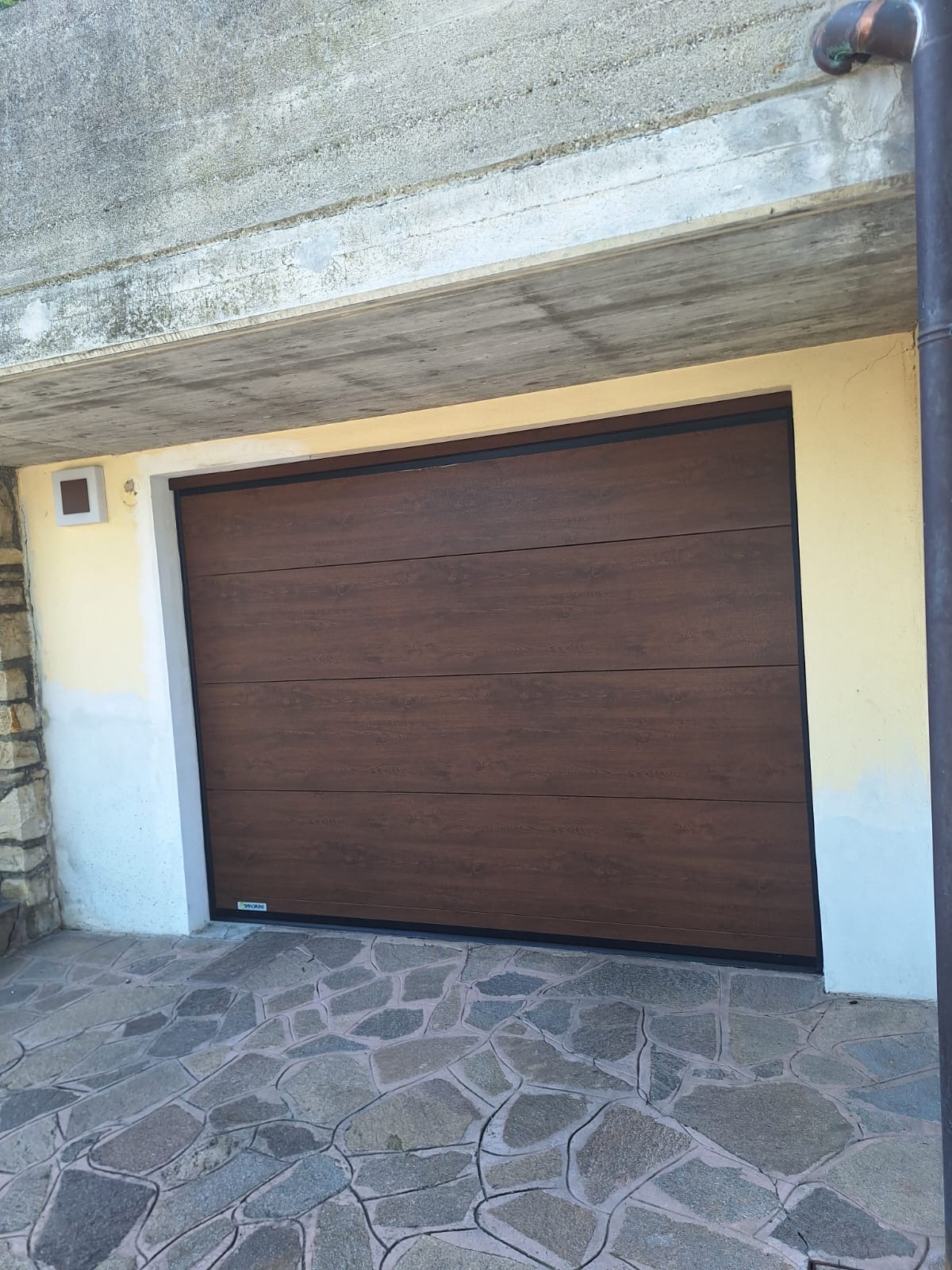Porta sezionale a <p>Porta sezionale oltre luce, con pannello intero. Colore effetto legno scuro </p>