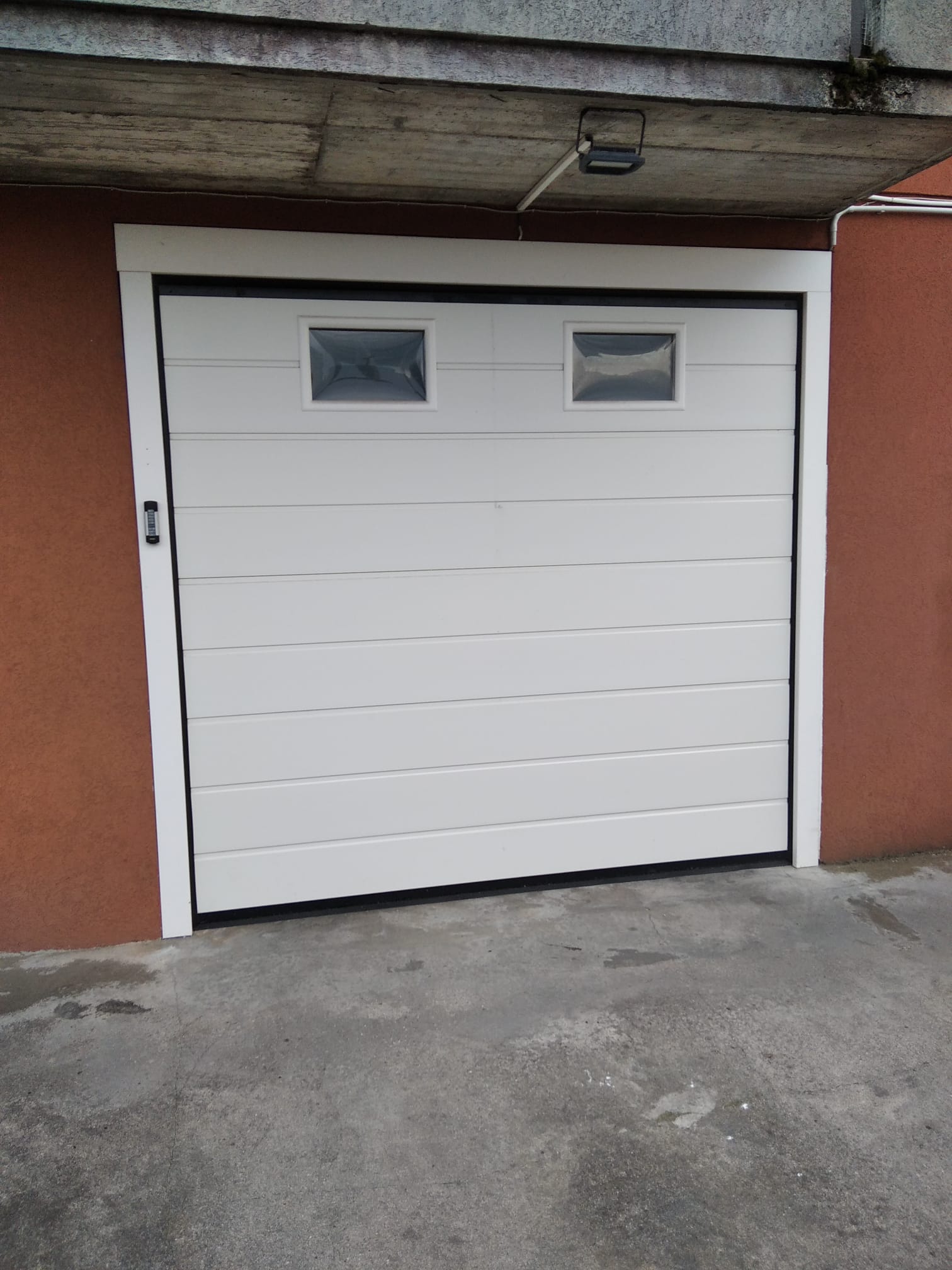 porta sezionale a <p>porta sezionale in luce, con oblò, telecodi e pannello con doga da 24cm. RAL 9010</p>