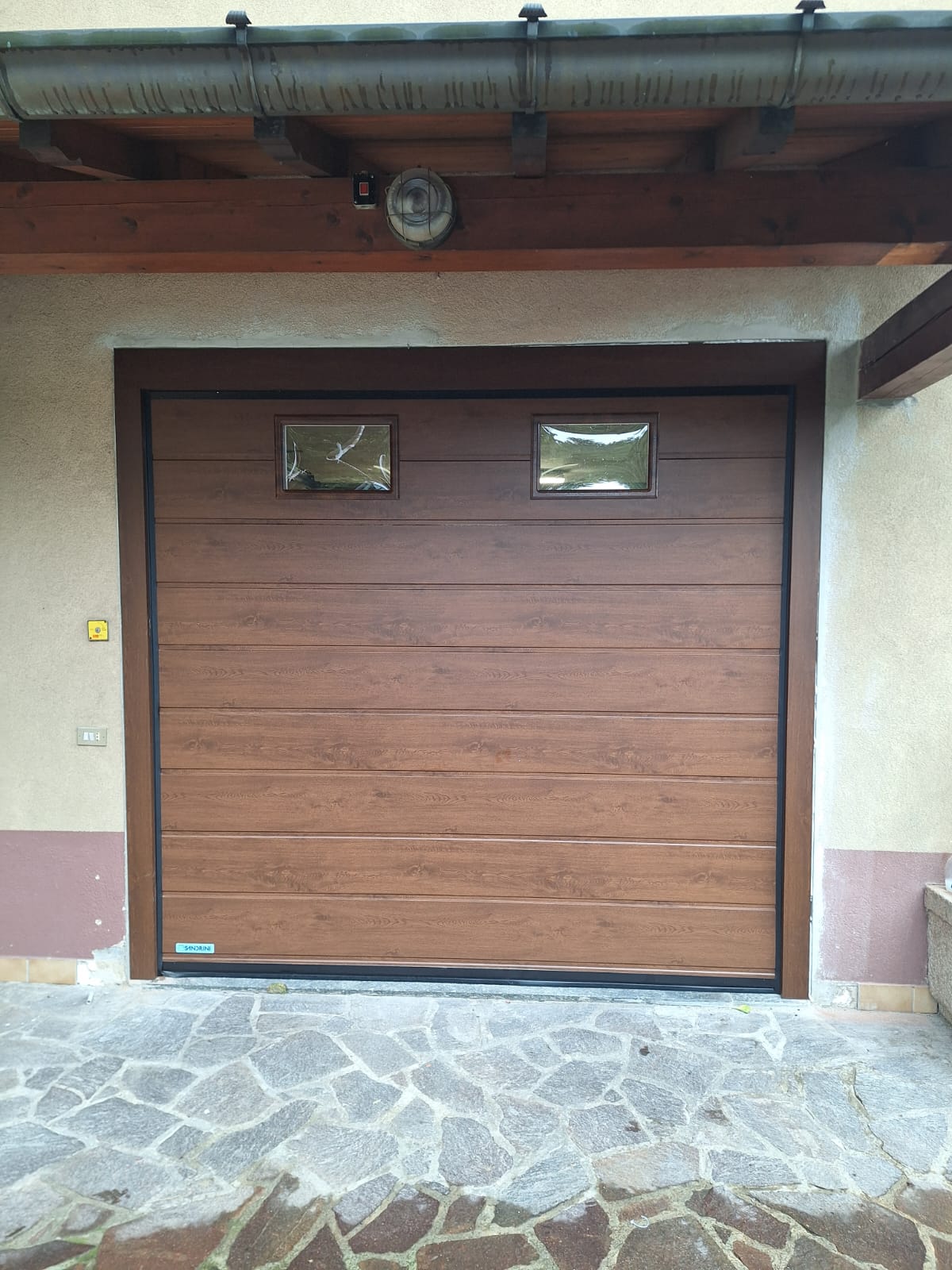 porta sezionale a <p>porta sezionale in luce, con oblò e pannello con doga da 25cm. colore effetto legno scuro </p>
